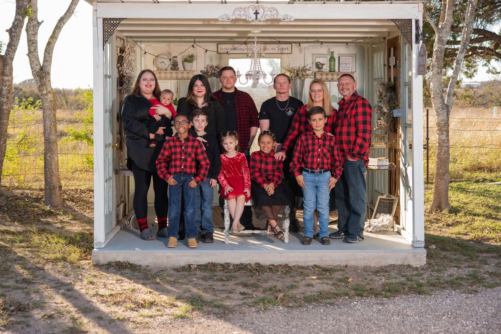 Large family in matching red plaid flannel shirts posing together in a rustic outdoor shed for a holiday portrait.