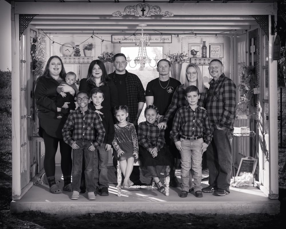 Black and white family portrait of multigenerational group with children in matching plaid shirts posing in garage doorway.