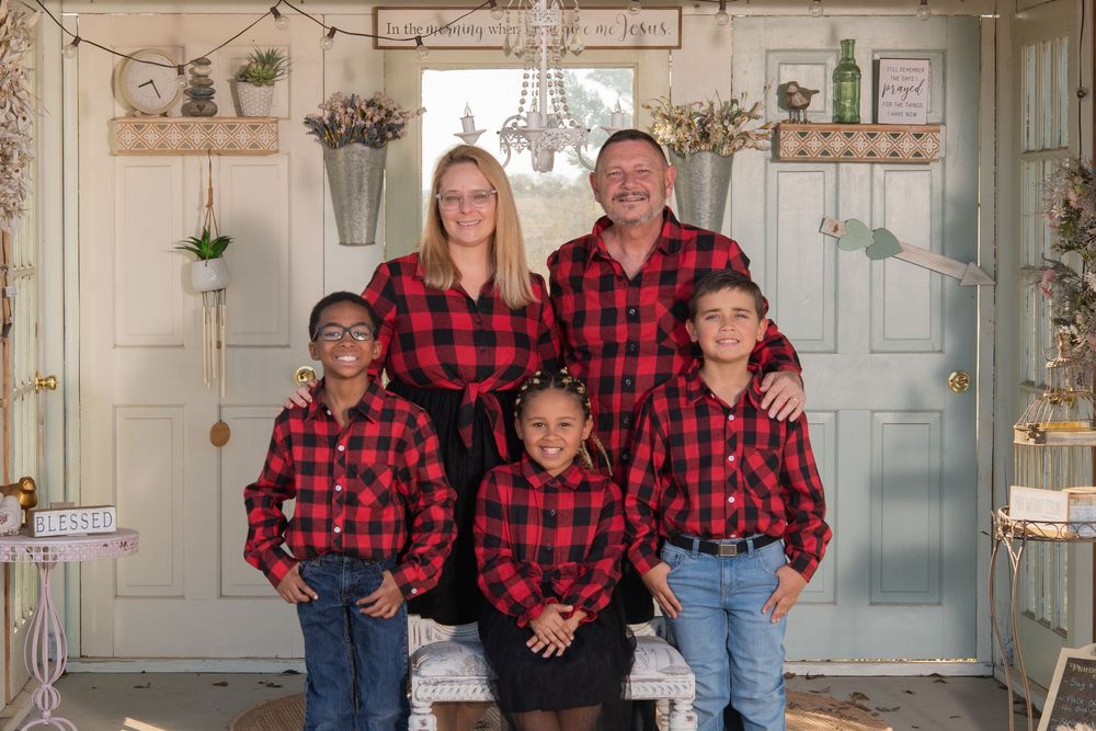 Family of five in matching red plaid shirts posing for a holiday portrait in a decorated vintage-style setting.