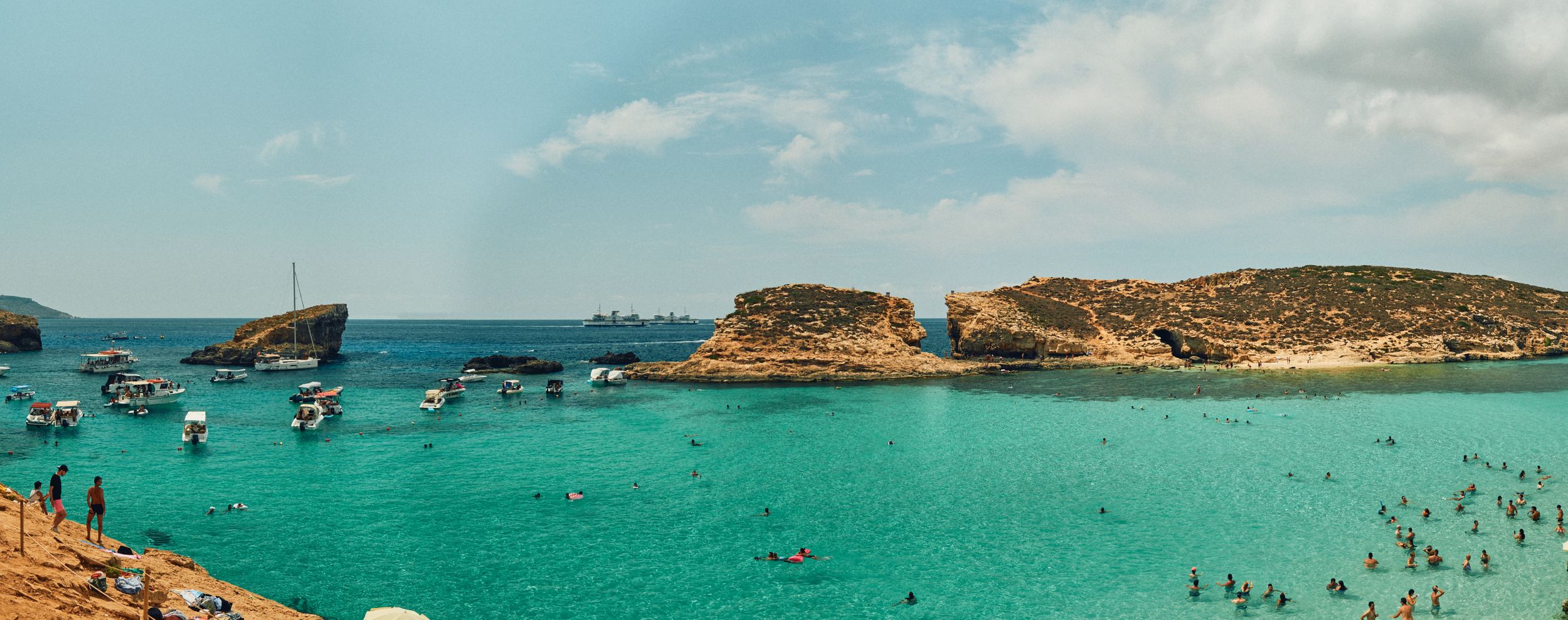 Panoramic view of Malta's Blue Lagoon with boats scattered across the crystal clear waters.