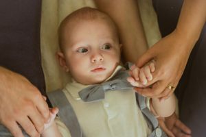 Baby wearing light colored outfit looking up while hands adjust their clothing.