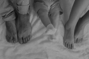 Black and white photo of feet resting together on white bedding.