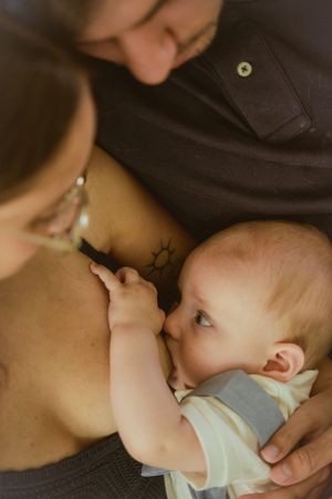 Intimate breastfeeding moment between parent and baby wearing light colored clothing.