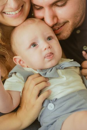 Close family portrait showing loving moment with baby in light colored outfit.