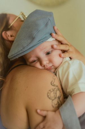Intimate moment showing a baby in blue cap being held close against someone with visible tattoo art.