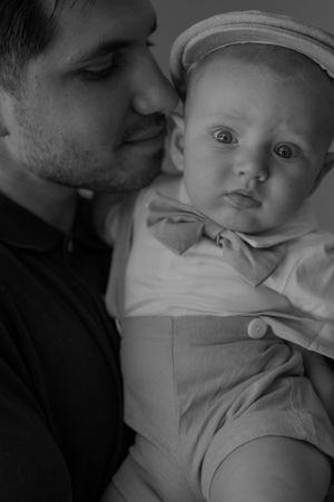 Black and white portrait of a baby in cap being held close.