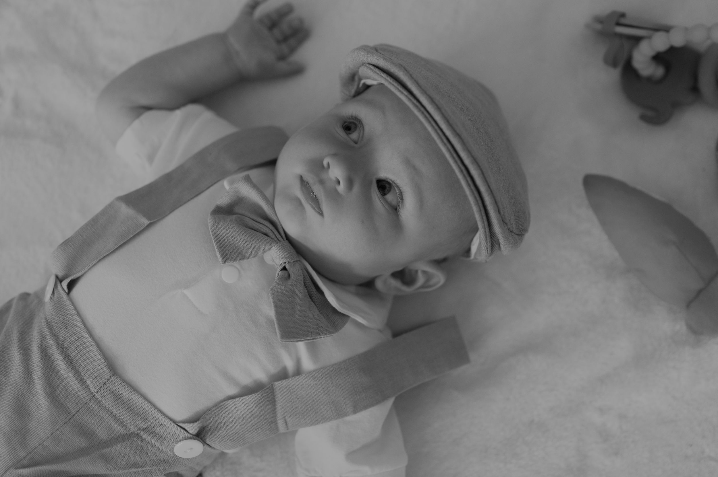 Baby in vintage-style black and white photo wearing a light colored outfit and cap while lying down.