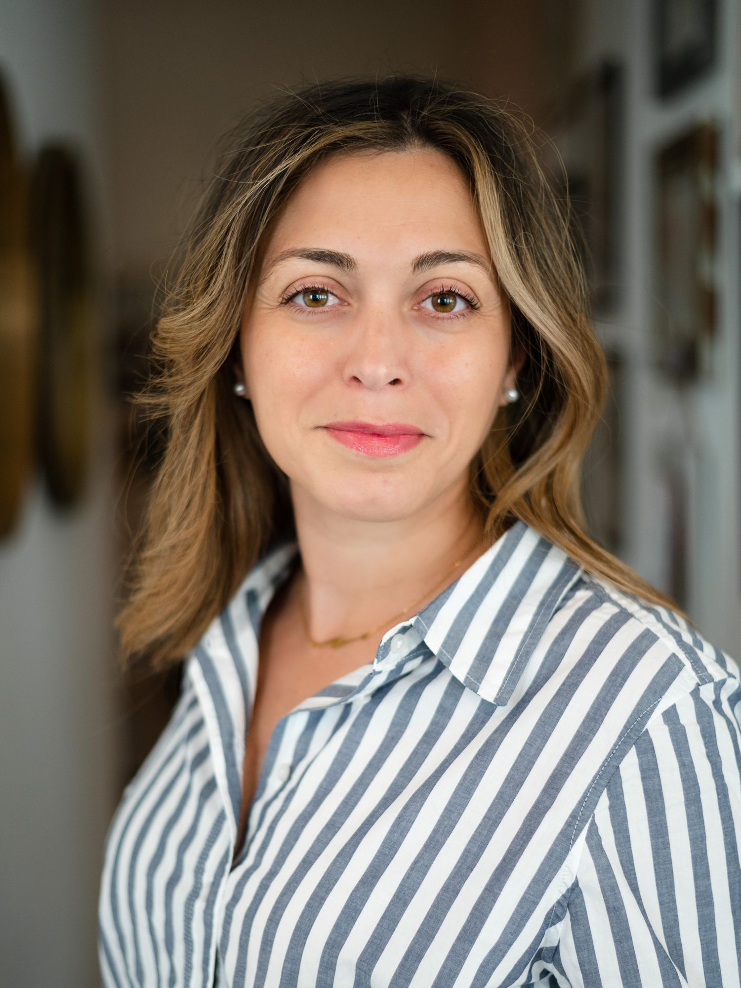 Professional portrait of person in striped button-down shirt against blurred interior background.