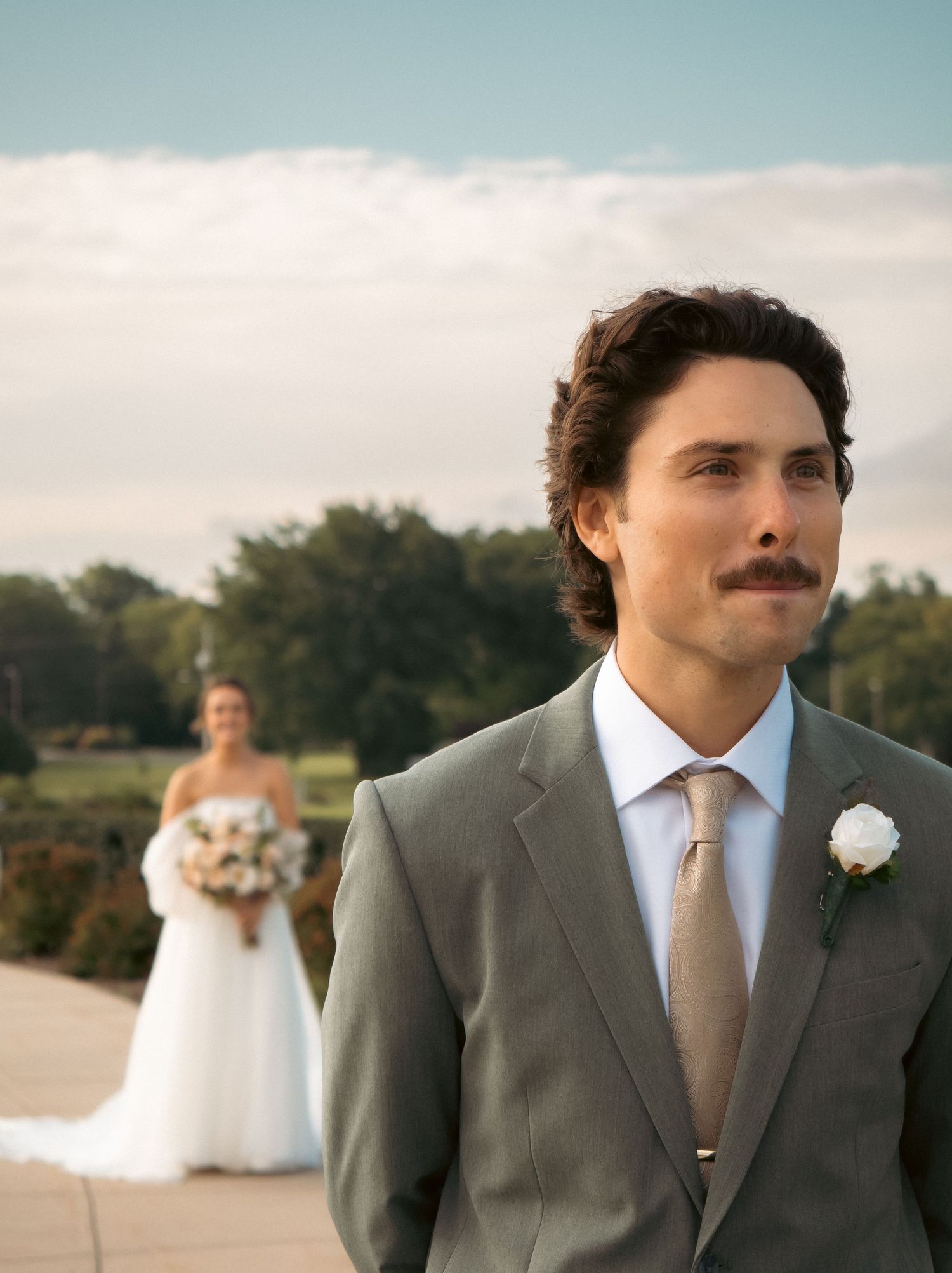 A wedding portrait with a groom in grey suit and bride in background.