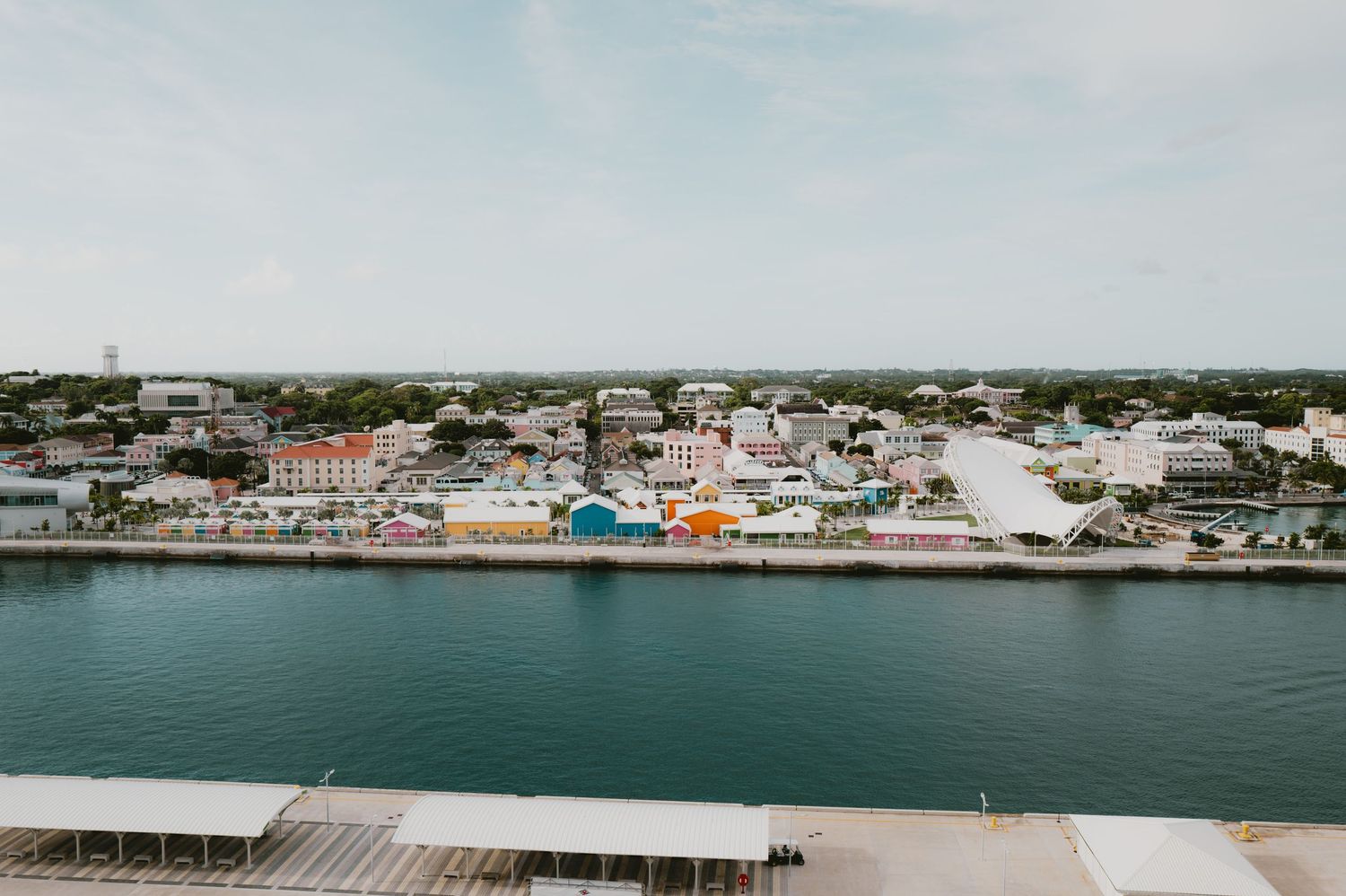 Aerial view of colorful coastal town buildings along waterfront with boats docked in blue harbor.