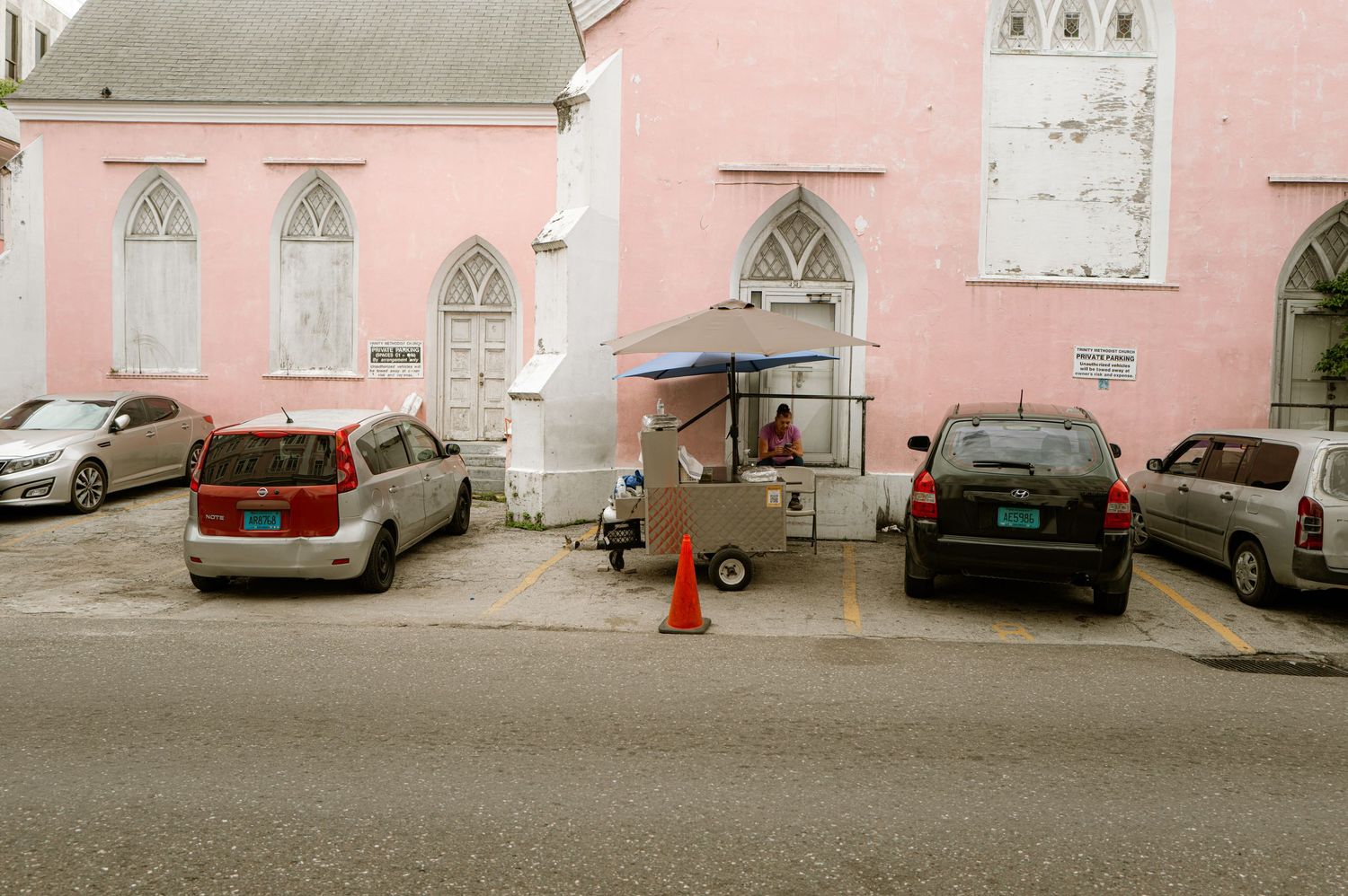 Pink church building exterior with Gothic windows and parked cars along street.