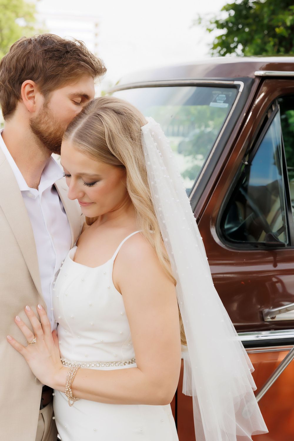 Tender embrace between couple against classic car during wedding photos.