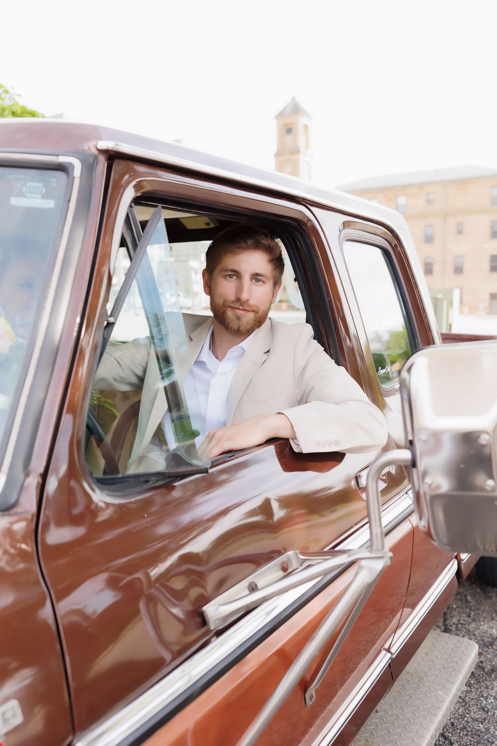 Person in light suit poses in driver's seat of classic brown Ford truck.