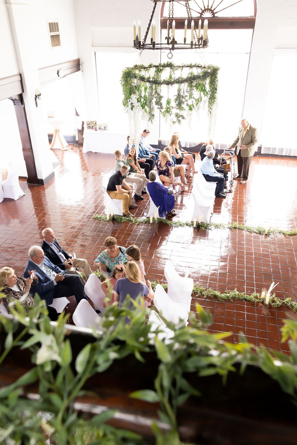 Overhead view of wedding ceremony seating with greenery chandeliers and brick flooring.