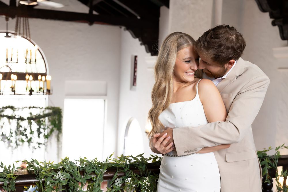 A romantic wedding couple embracing under a chandelier with decorative greenery garlands.