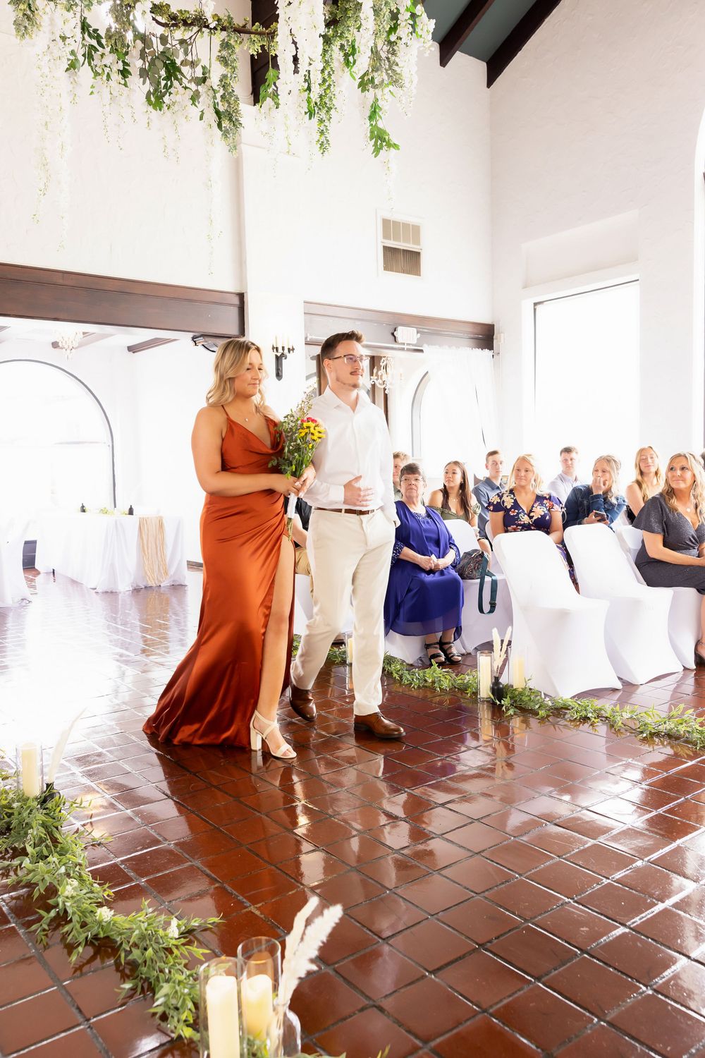 Wedding party members entering a decorated reception hall with terracotta tiles and hanging greenery.