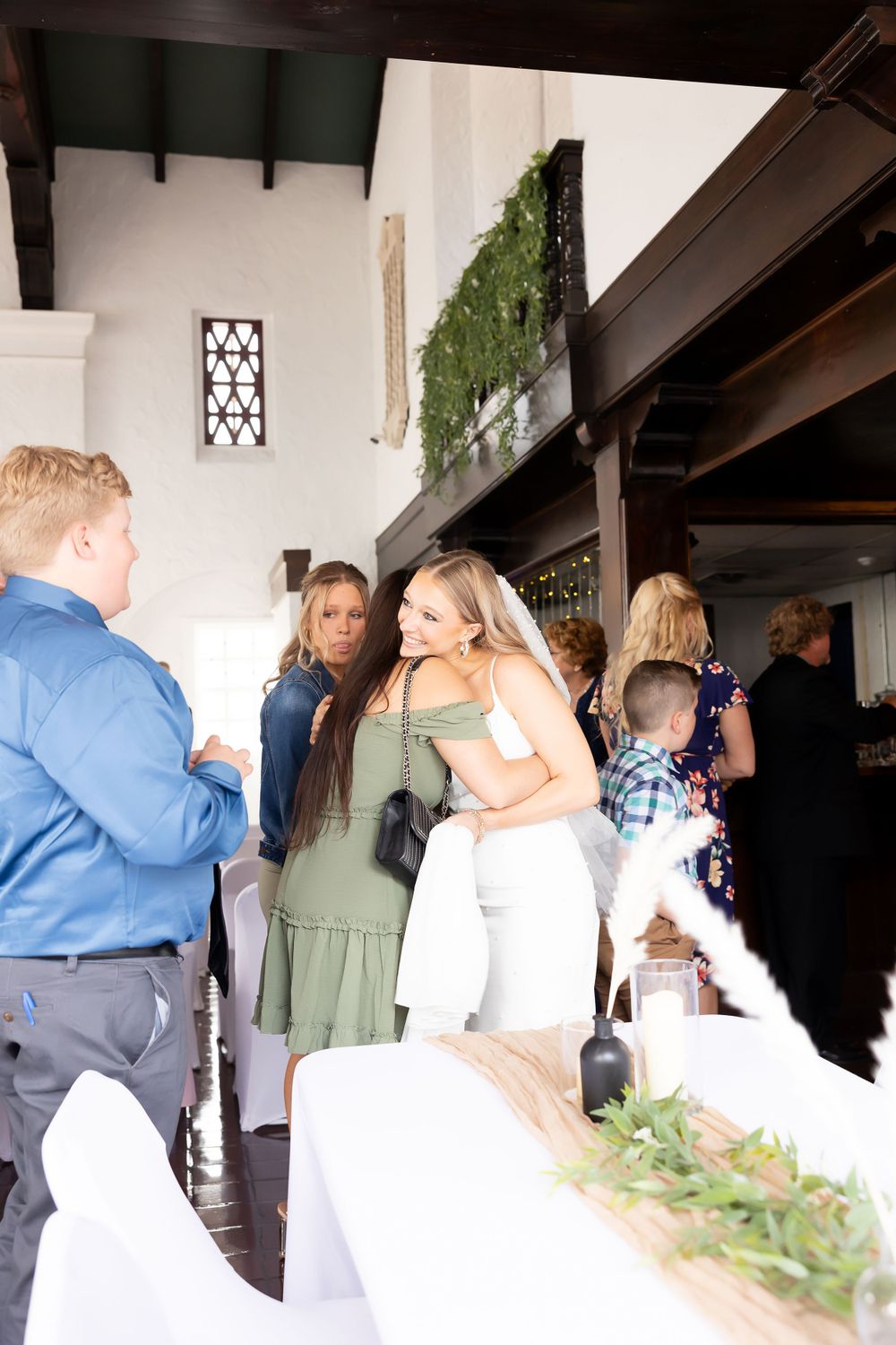Wedding reception guests gather in an elegant Spanish-style venue with white walls and greenery.