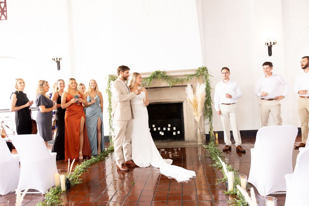 Wedding ceremony in elegant white room with decorated fireplace and white chairs.