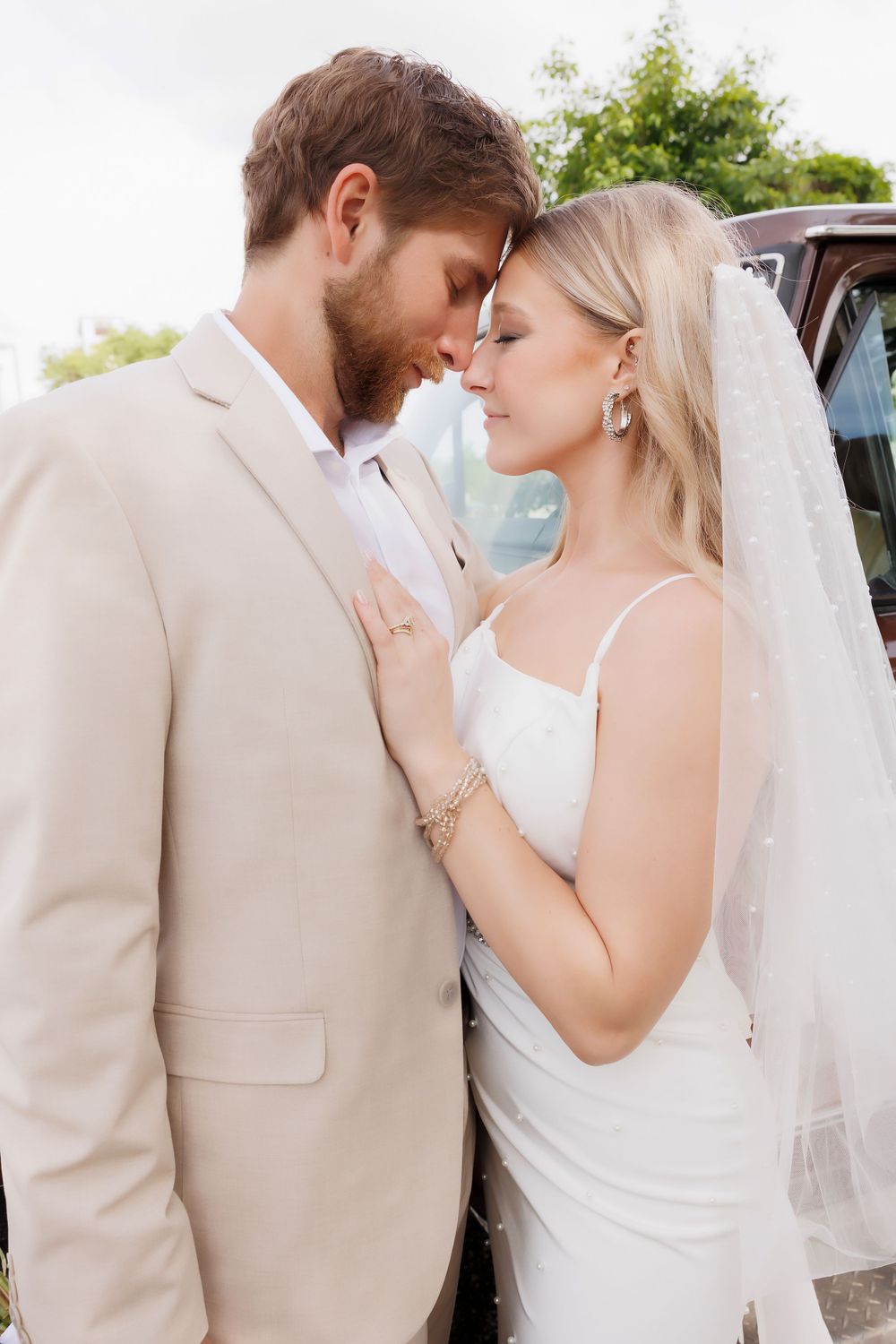A romantic wedding moment between a couple in beige and white against a sunny outdoor backdrop.