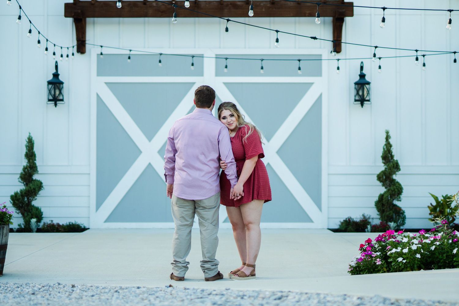 A couple poses against a white barn door with string lights and lanterns.
