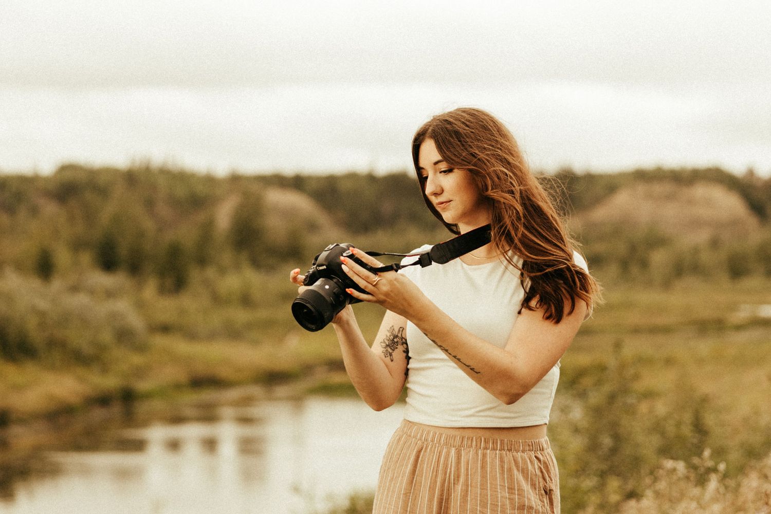 Brunette girl standing outside near river looking down at her camera.