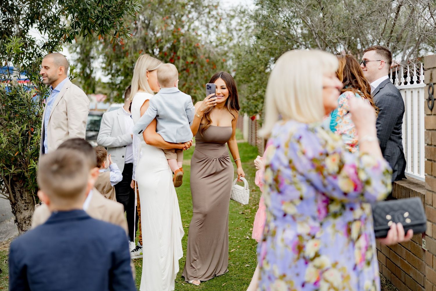 Wedding guests gathering outdoors in formal attire at garden reception.