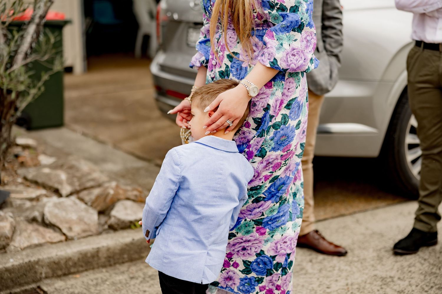 A colorful floral dress is seen as someone interacts with a small child in a blue shirt outdoors.