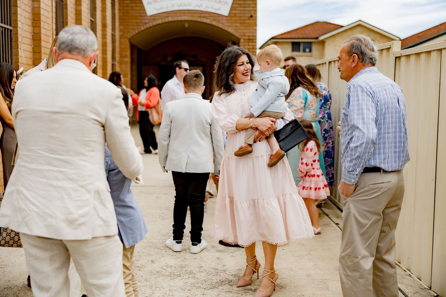 A gathering of guests in formal attire outside a church building.
