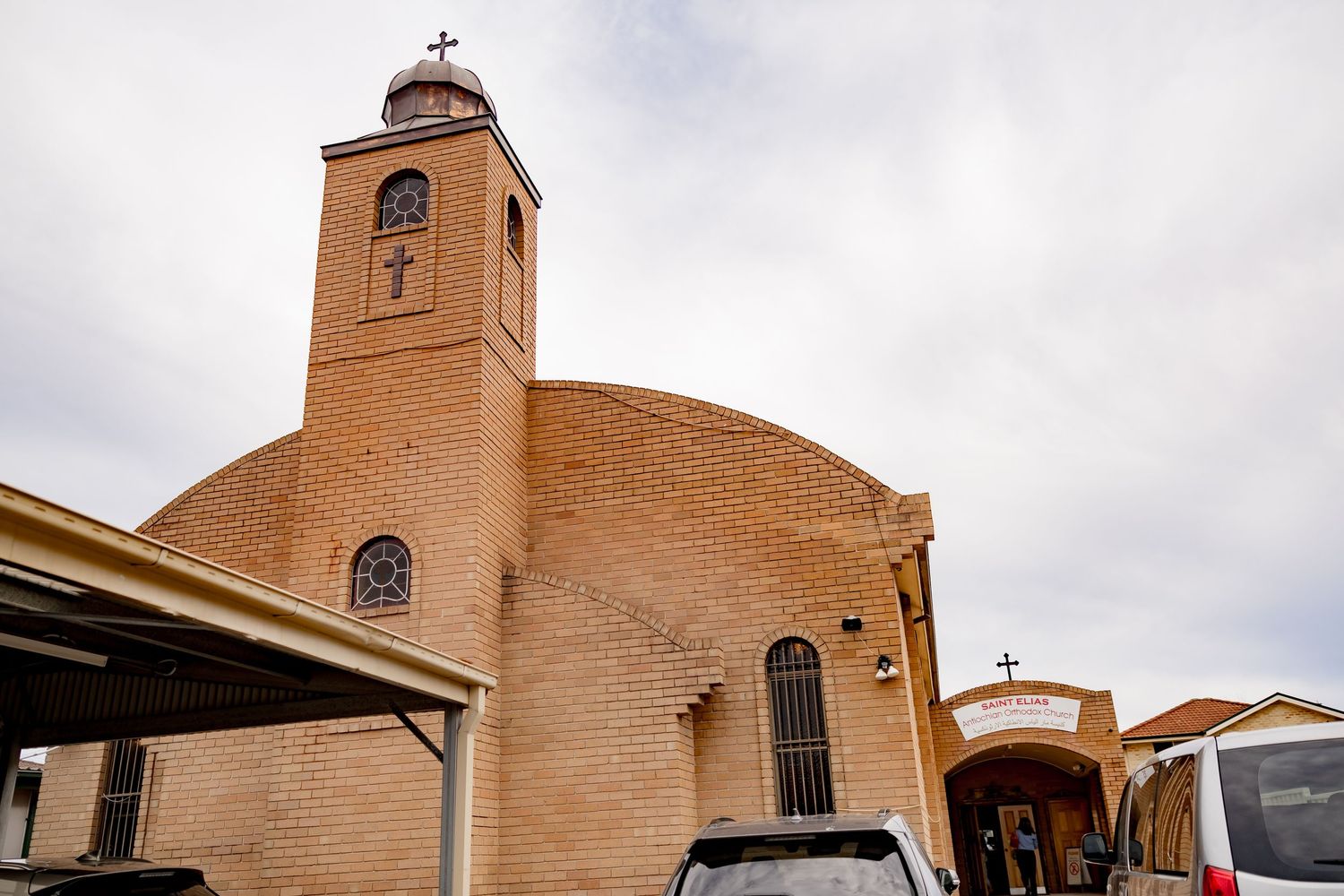 Exterior view of a brick church building with bell tower under cloudy skies.