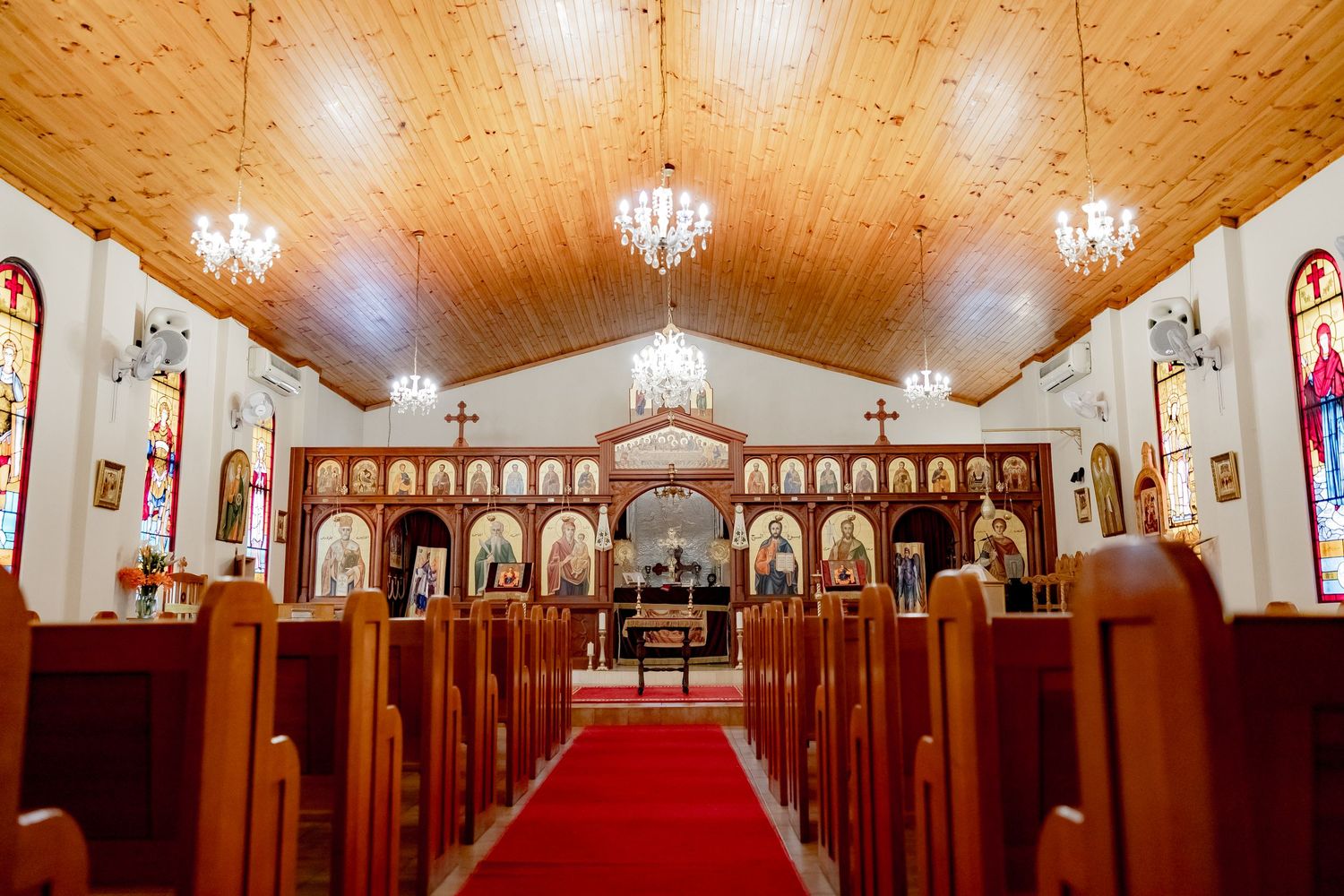 Interior of orthodox church with wooden ceiling, chandeliers and red carpet aisle.