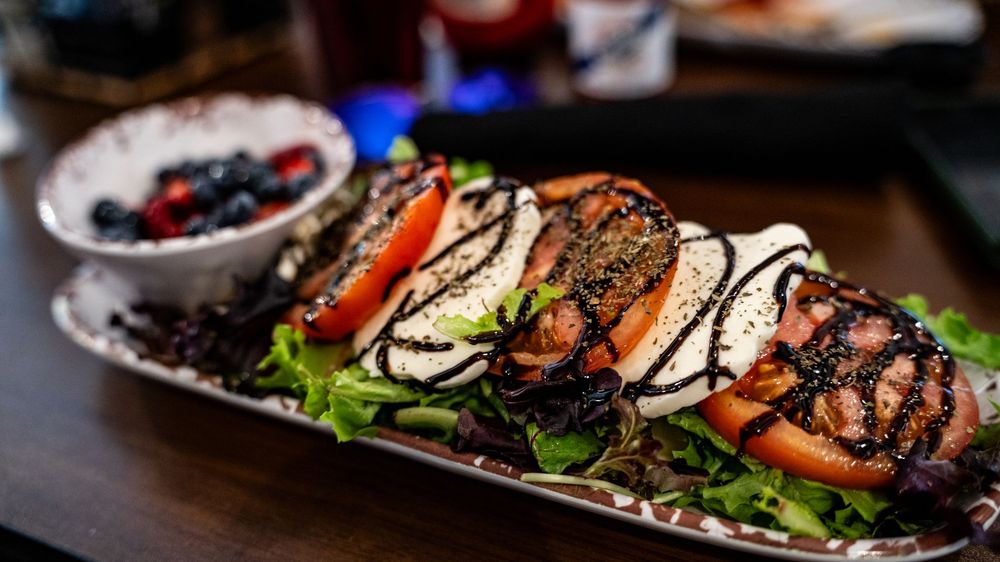 Grilled chicken sandwich with balsamic drizzle, tomatoes and lettuce served on a dark plate with mixed berries.