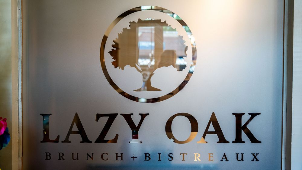 Illuminated restaurant sign for Lazy Oak Brunch Bistro glows against dark background.