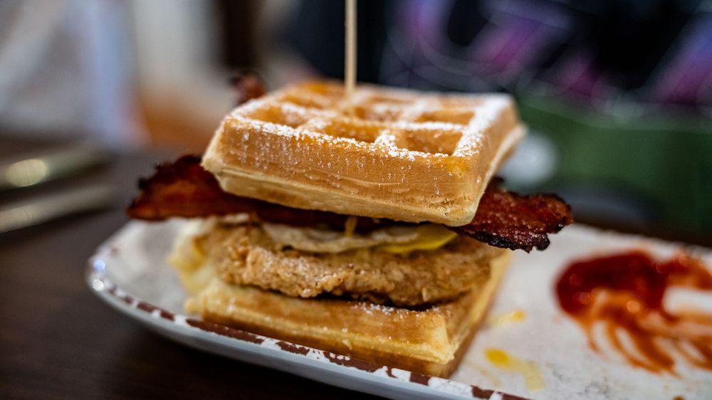 A collage of golden brown waffles topped with syrup, butter, and various breakfast toppings on white plates.