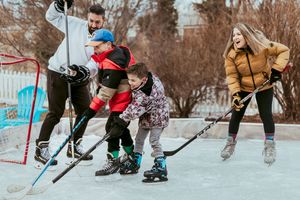 Group of people enjoying winter fun while playing ice hockey and skating on an outdoor rink in cold weather.