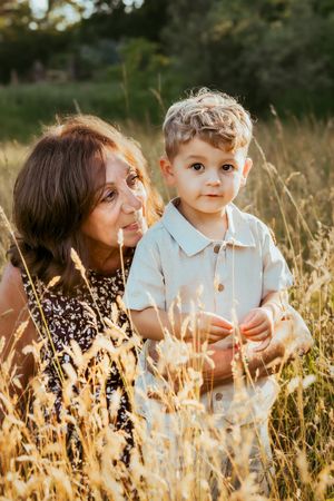 Mother and child sharing tender moments lying in golden sun-lit field of tall grass at sunset.
