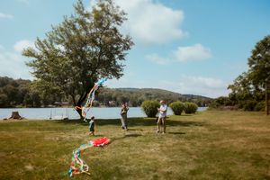 People enjoying a summer day by the lake with a grassy field and trees under blue skies.