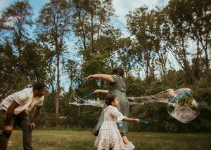 A couple dances together in a sunny field surrounded by autumn trees during a romantic photoshoot.