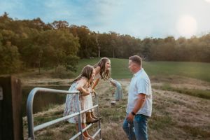 A golden hour maternity photoshoot featuring silhouettes by a rustic fence in a pastoral setting.