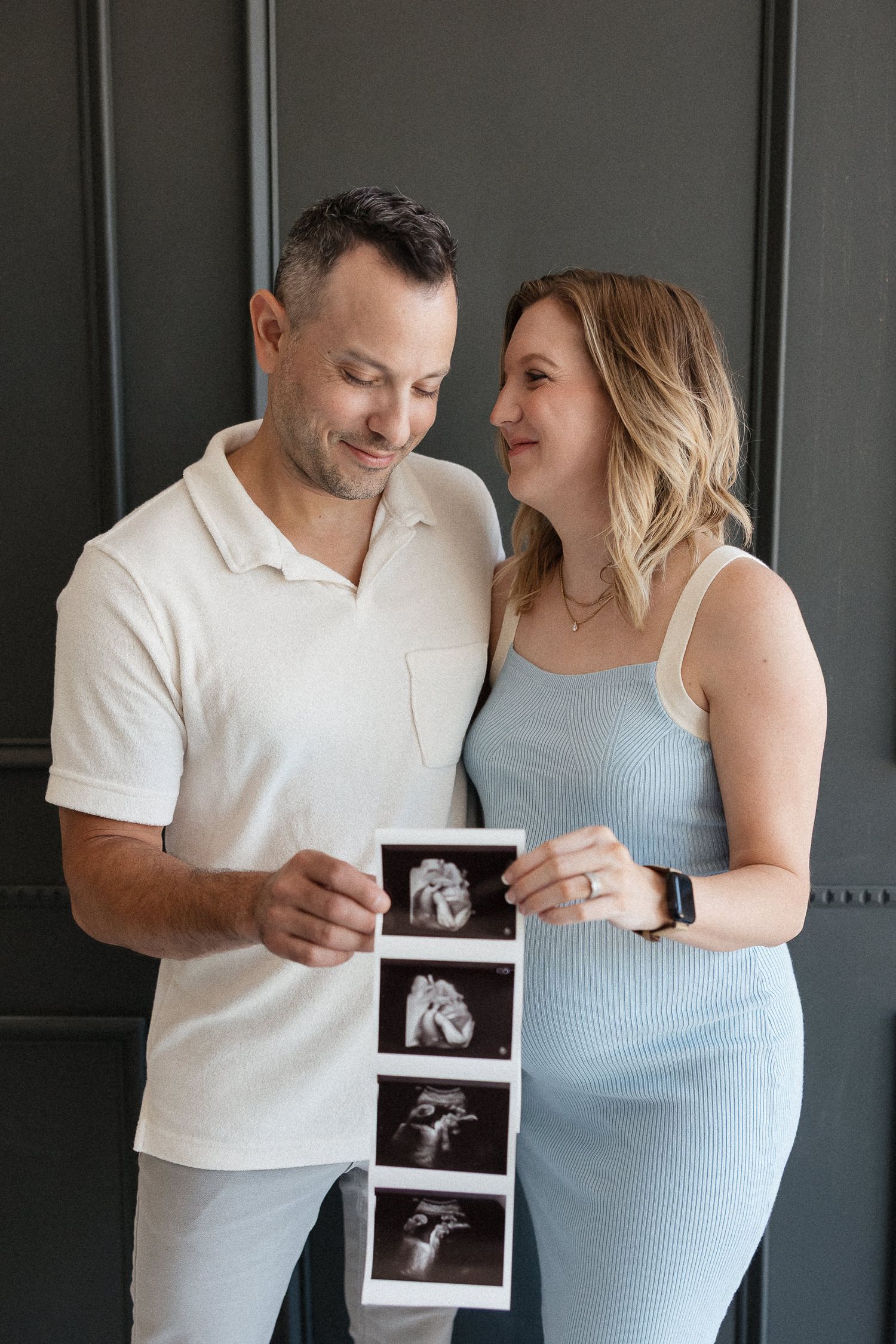 pregnant couple holding sonogram image smiling at one another during kansas city newborn photographer session
