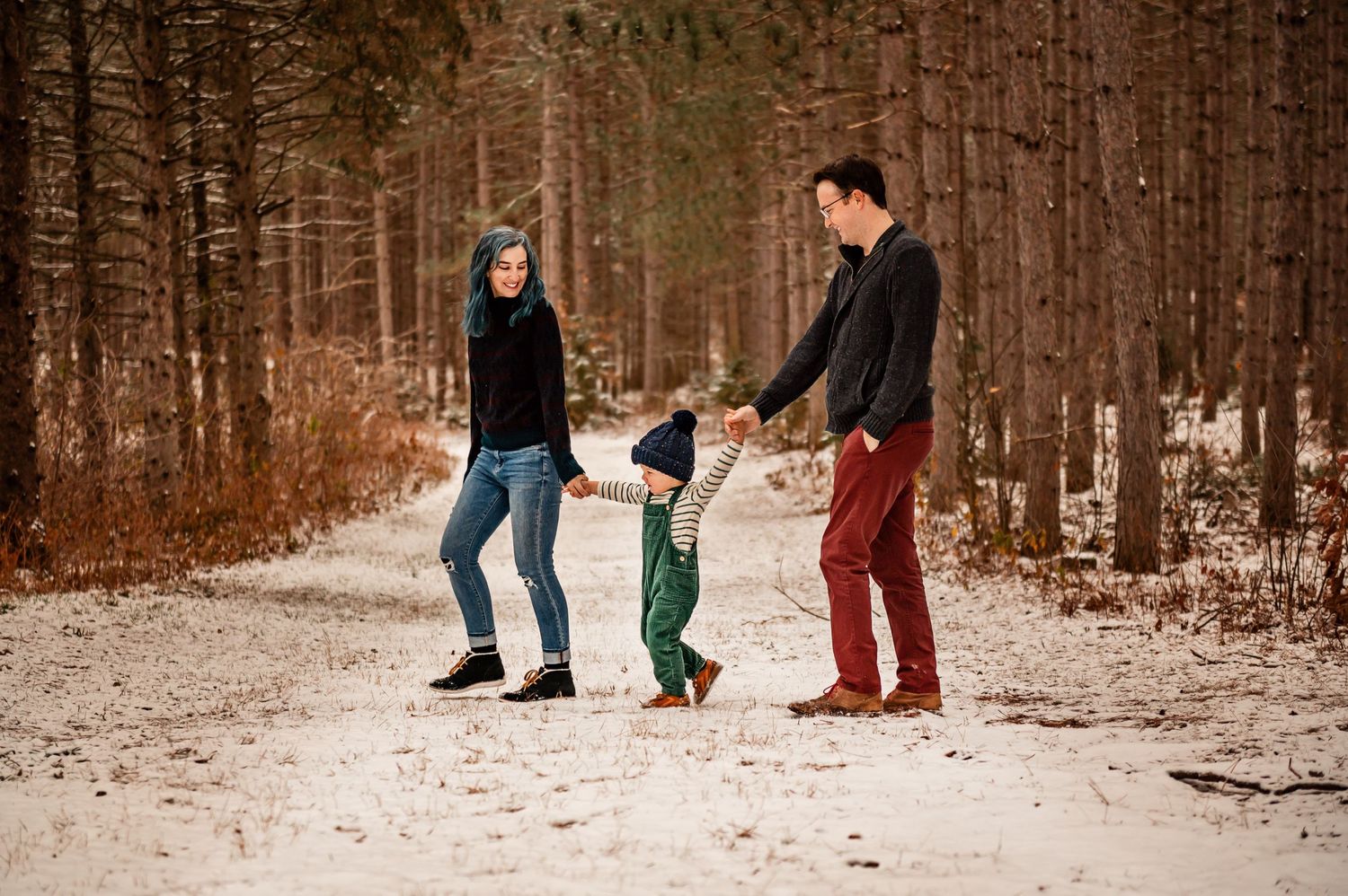 Family holding hands and walking together on a snowy forest trail.