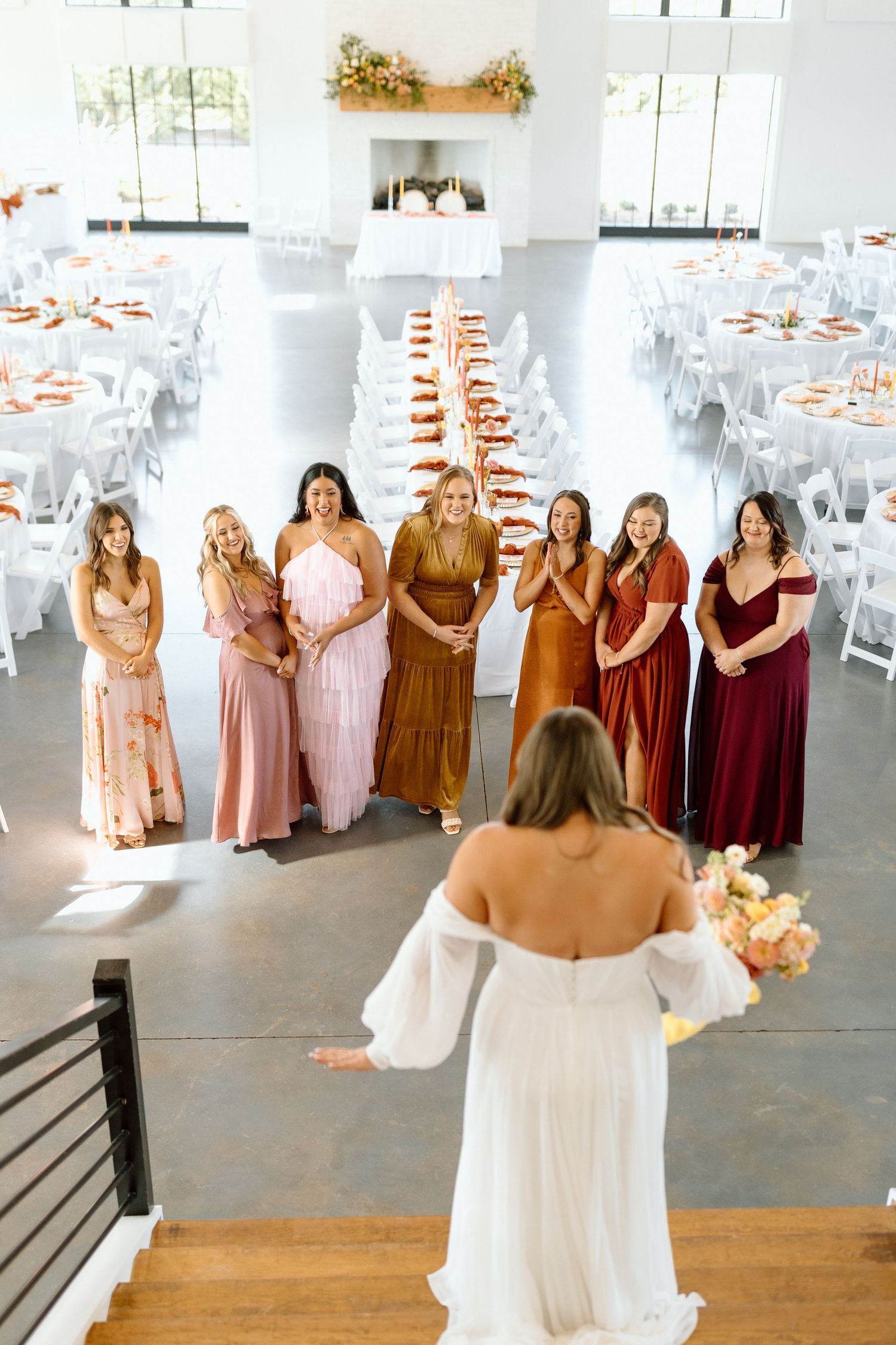 Wedding scene with bridesmaids in pink and burgundy dresses watching bride on stairs.