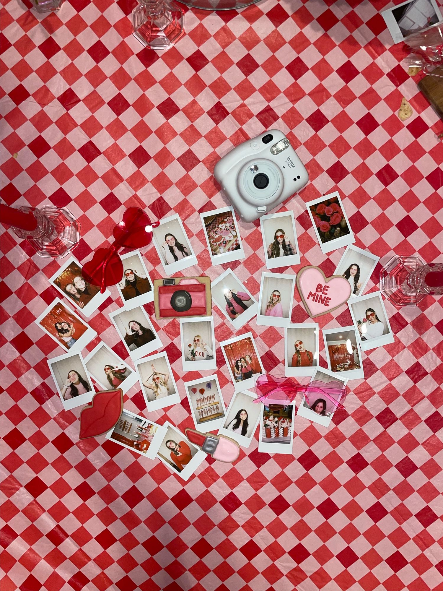Instax camera and polaroid photos scattered on red and white checkered picnic blanket.