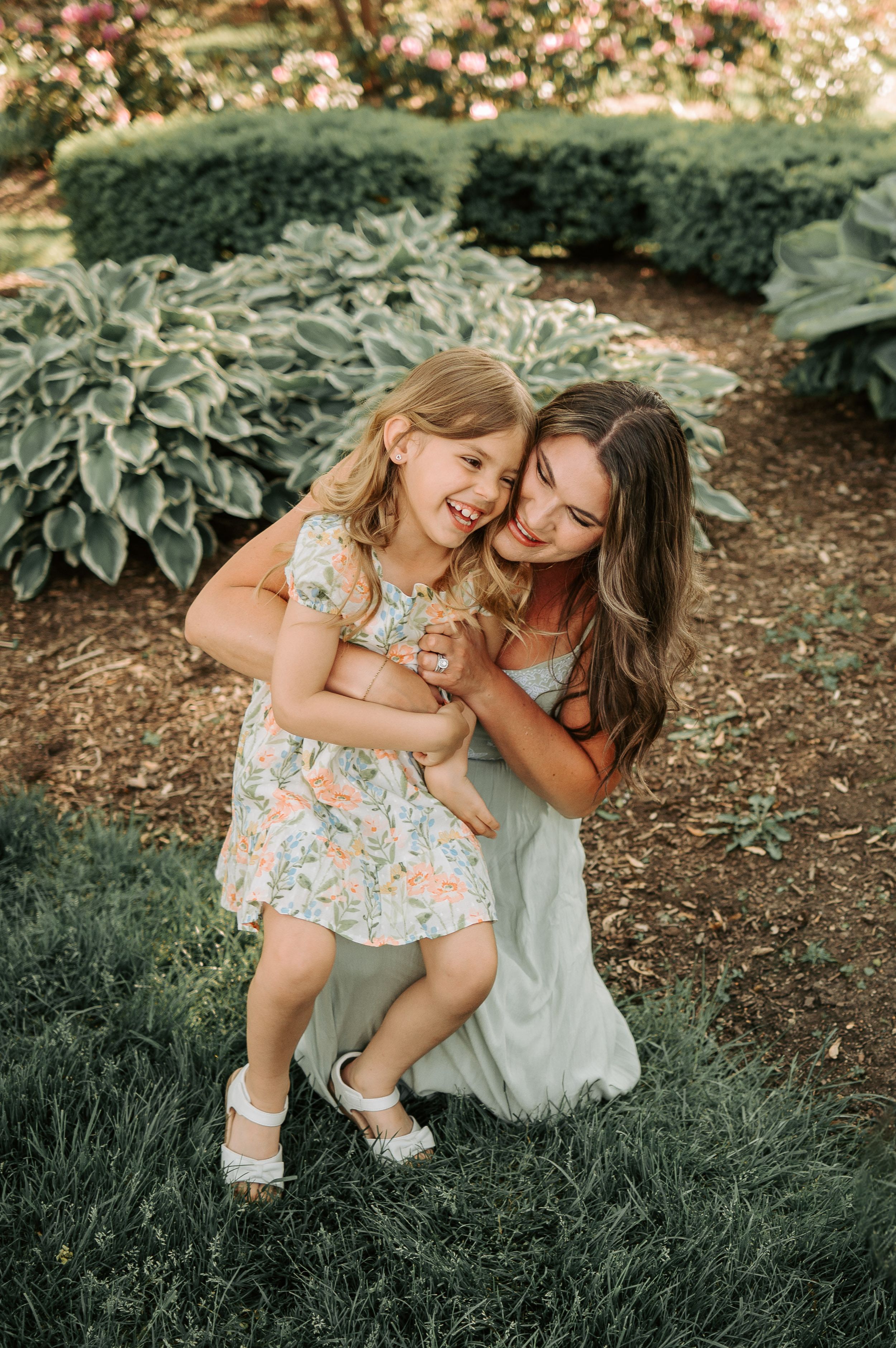 Joyful moment captured in a garden with lush hostas and flowering trees in the background during golden hour.