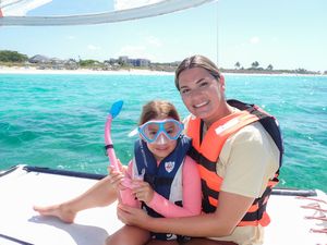 Two people wearing life jackets smile while enjoying a boat trip on bright turquoise tropical waters.