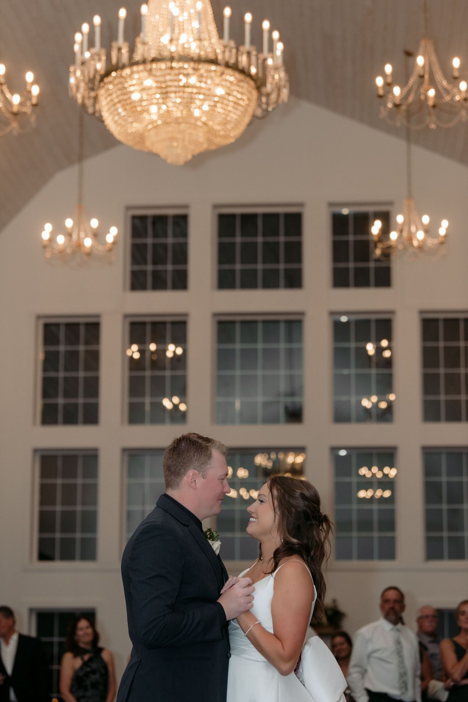 bride and groom dancing during their first dance with chandeliers sparkling overhead at abella farms ballroom in chisago city, mn.