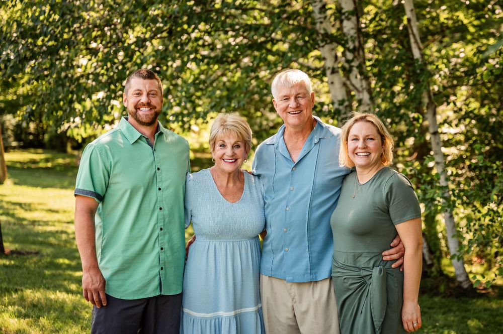 Four family members pose together for portrait in sunlit garden setting.