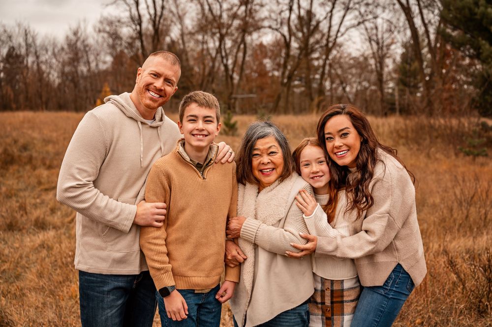 A family group poses together outdoors in a golden autumn field wearing coordinated neutral colored clothing.