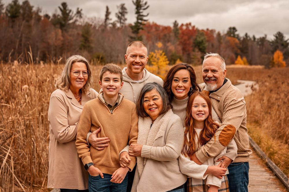 A family in neutral-toned clothing poses together outdoors during autumn with golden grass and trees in the background.