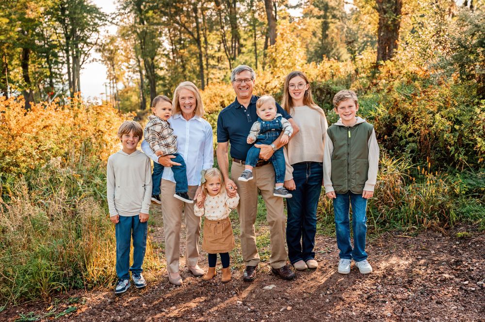 Large family group poses together on an autumn trail with golden foliage in the background.
