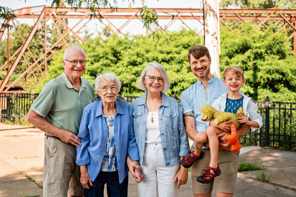 Three generations gather for outdoor family photo under red pergola structure.